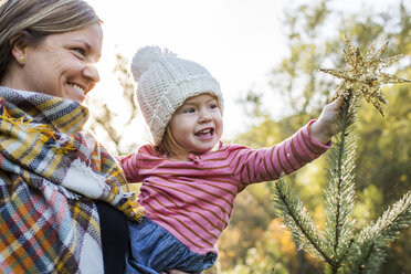 Kaukasische Mutter hilft ihrer Tochter, einen Stern auf die Spitze des Weihnachtsbaums zu setzen - BLEF00310