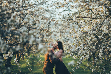 Kaukasisches Paar, das sich in der Nähe blühender Bäume küsst - BLEF00376
