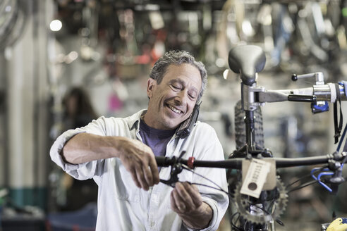 Caucasian man talking on telephone and repairing brakes on bicycle - BLEF00433