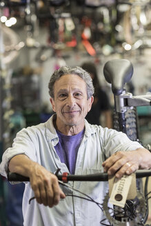Portrait of smiling Caucasian man leaning on bicycle in shop - BLEF00434