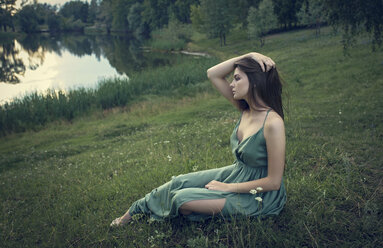 Kaukasische Frau sitzt im Gras mit Wildblumen in der Nähe eines Sees - BLEF00484
