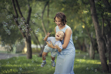 Kaukasische Mutter hält ihren kleinen Sohn und spielt mit Seifenblasen - BLEF00488