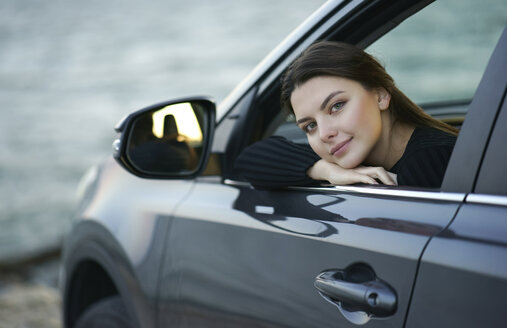 Lächelnde kaukasische Frau, die sich in ein Autofenster lehnt - BLEF00494