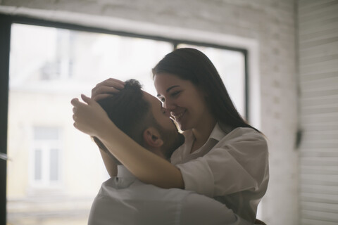 Kaukasisches Paar umarmt sich am Fenster, lizenzfreies Stockfoto