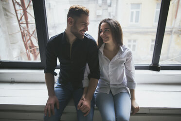 Caucasian couple sitting on window sill holding hands - BLEF00548