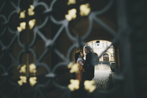 Kaukasisches Paar, das sich auf der Straße hinter einem Tor umarmt - BLEF00581