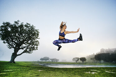 Gemischtrassige Frau, die in der Nähe eines Sees trainiert und springt - BLEF00633