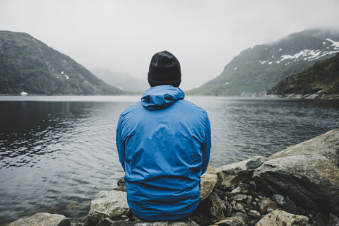 Kaukasischer Mann sitzt auf Felsen und bewundert den See, lizenzfreies Stockfoto