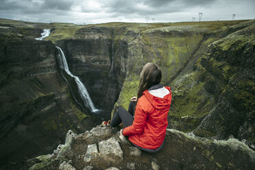 Kaukasische Frau sitzt auf einer Klippe und bewundert einen Wasserfall - BLEF00724