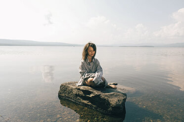 Kaukasisches Mädchen sitzt auf einem Felsen im See - BLEF00757