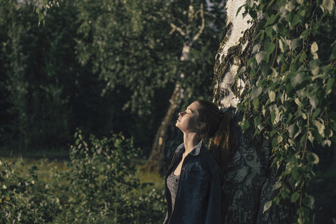 Kaukasische Frau lehnt sich an einen Baumstamm, lizenzfreies Stockfoto