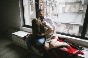 Caucasian couple cuddling on bench near window - BLEF00799