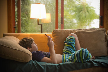 Kaukasischer Junge liegt auf dem Sofa und schreibt eine SMS auf seinem Handy - BLEF00843