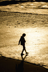 Silhouette eines gemischtrassigen Jungen, der bei Sonnenuntergang am Strand spazieren geht - BLEF00845