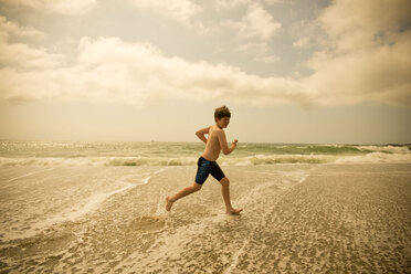 Caucasian boy running in ocean waves - BLEF00848