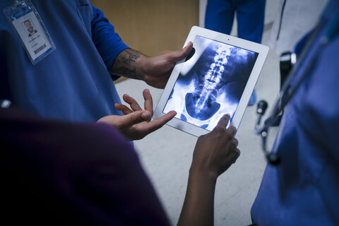 Ärzte untersuchen Röntgenaufnahmen von Becken und Wirbelsäule auf einem digitalen Tablet, lizenzfreies Stockfoto