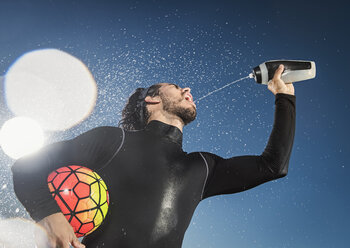Hispanischer Mann, der einen Fußball hält und sich Wasser in den Mund spritzt - BLEF01017