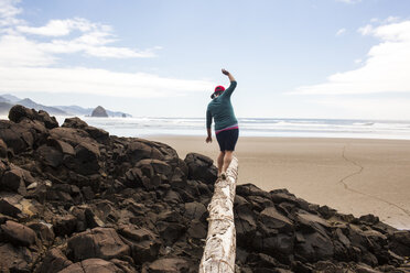 Caucasian woman balancing on log on rocks at beach - BLEF01059