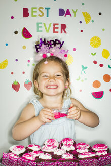 Kaukasisches Mädchen hält Streusel über einem Tablett mit Cupcakes zum Geburtstag - BLEF01075