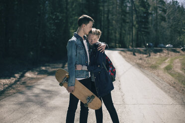 Caucasian couple with skateboard hugging in road - BLEF01082