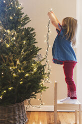 Kaukasisches Mädchen hängt Lichter am Weihnachtsbaum auf - BLEF01093