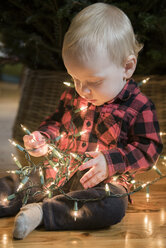 Caucasian baby boy sitting on floor wrapped in string lights - BLEF01097