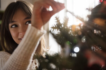 Mixed Race woman placing tinsel on Christmas tree - BLEF01098