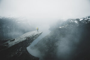Kaukasischer Mann auf einer nebligen Klippe, der die malerische Aussicht auf einen Bergfluss bewundert - BLEF01130