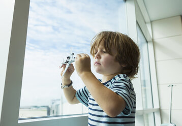 Kaukasischer Junge spielt mit Spielzeugflugzeug in der Nähe des Fensters - BLEF01159