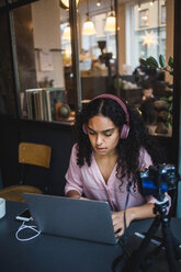 Selbstbewusste junge Influencerin mit Laptop beim Vloggen am Schreibtisch im Kreativbüro - MASF11886