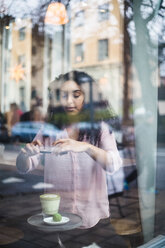 Junge Influencerin fotografiert Tee und Snack auf dem Tisch mit dem Smartphone durch das Fenster gesehen - MASF11910