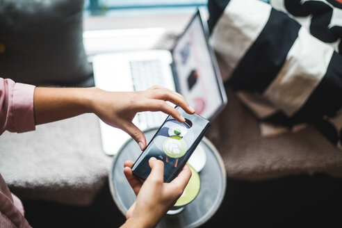 Hohe Winkel Ansicht der weiblichen Blogger fotografieren Matcha Tee und Snack durch Smartphone im kreativen Büro - MASF11918