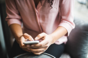 Mittelteil einer jungen Geschäftsfrau, die mit ihrem Smartphone im Kreativbüro Textnachrichten verschickt - MASF11921