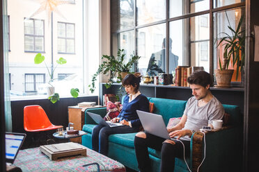 Multiethnische männliche und weibliche Berufstätige mit Laptops auf dem Sofa im Büro sitzend - MASF11932