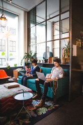 Confident multi-ethnic male and female professionals using laptops sitting on sofa at office - MASF11933