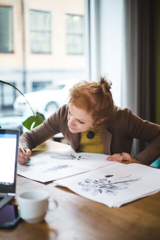 Selbstbewusste Illustratorin, die an einem Tisch im Büro auf Papier zeichnet, lizenzfreies Stockfoto