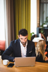 Confident male entrepreneur using laptop while sitting at table in office - MASF11959