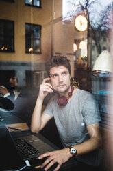 Nachdenklicher männlicher Unternehmer, der mit einem Laptop sitzt und durch ein Fenster im Büro schaut - MASF11960