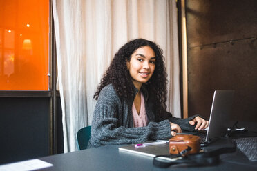 Porträt einer lächelnden Jungunternehmerin, die mit einem Laptop am Schreibtisch im Büro sitzt - MASF11962