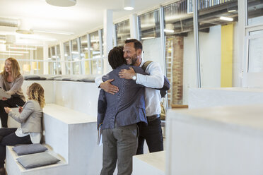 Smiling businessman embracing male colleague while standing in office - MASF11976