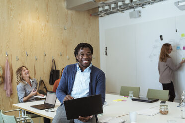 Smiling young businessman using laptop at conference table in board room - MASF11991