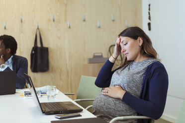 Müde schwangere Fachkraft, die in einer Bürobesprechung auf ihren Laptop schaut - MASF12002