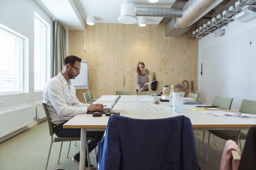 Mature businessman using laptop at conference table with coworker in background - MASF12009