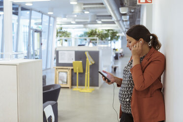 Schwangere Geschäftsfrau hört Musik auf ihrem Smartphone am Arbeitsplatz - MASF12018