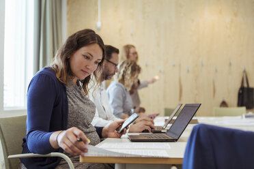 Schwangere Geschäftsfrau mit Smartphone und Laptop beim Lesen von Dokumenten in einer Bürobesprechung - MASF12021