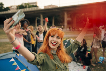 Glückliche junge Frau, die beim Camping während eines Musikfestivals ein Selfie mit Freunden macht - MASF12051