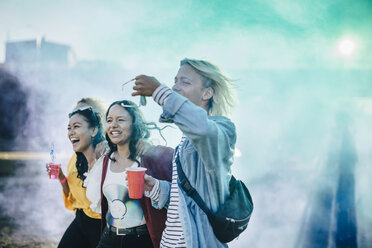 Fröhliche Freunde genießen Getränke beim Spaziergang inmitten von Pulverfarbe auf einem Musikfestival - MASF12060