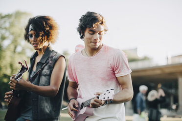 Glückliche junge Männer spielen Ukulele bei einem Musikkonzert im Sommer - MASF12072