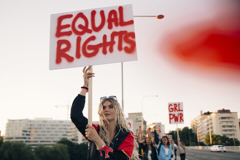 Women protesting with friends for equal rights in city against sky stock photo