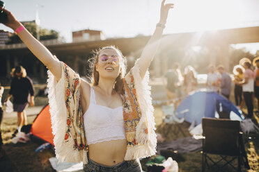 Happy young woman with arms raised enjoying at music event during summer - MASF12103